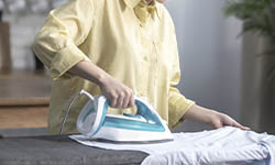 roupas-passadas: close em uma mesa de passar roupas com uma mulher de camisa amarela segurando o ferro azul e branco